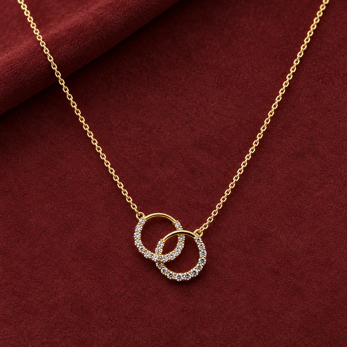 Gold-tone 316L stainless steel necklace with two interlocked open rings set with clear crystals on a fine cable chain, laid flat on a red cloth