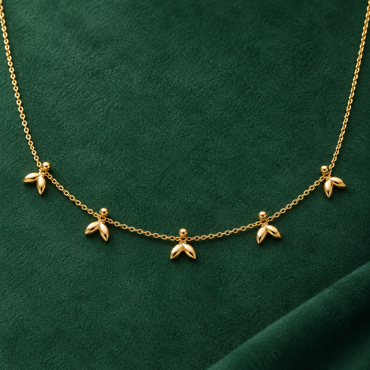 Gold-tone 316L stainless steel necklace with a fine cable chain and five small leaf-cluster drops, shown laid flat on green velvet