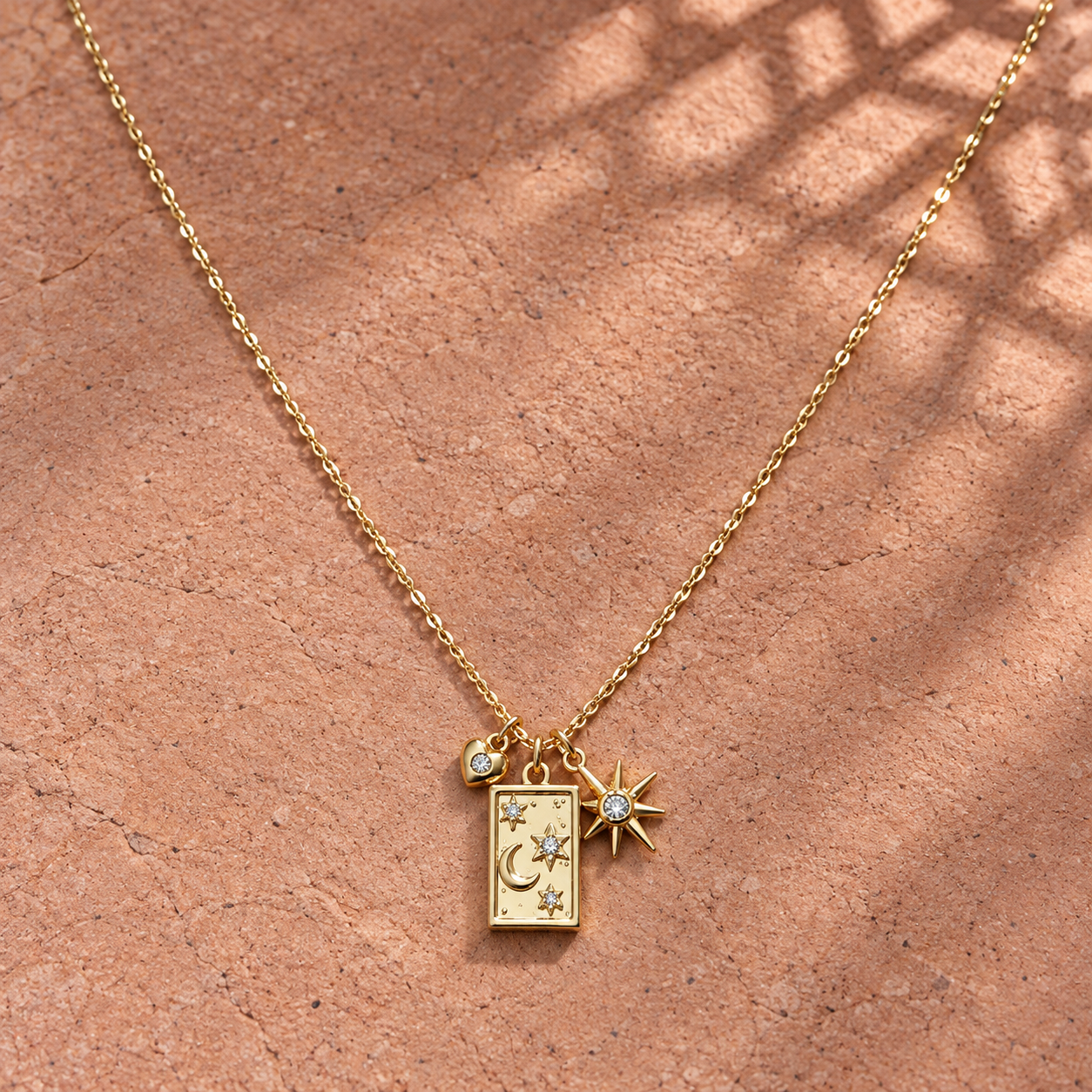 Gold-tone 316L stainless steel necklace with a rectangular charm engraved with moon and stars, plus a crystal-set star and small crystal bead