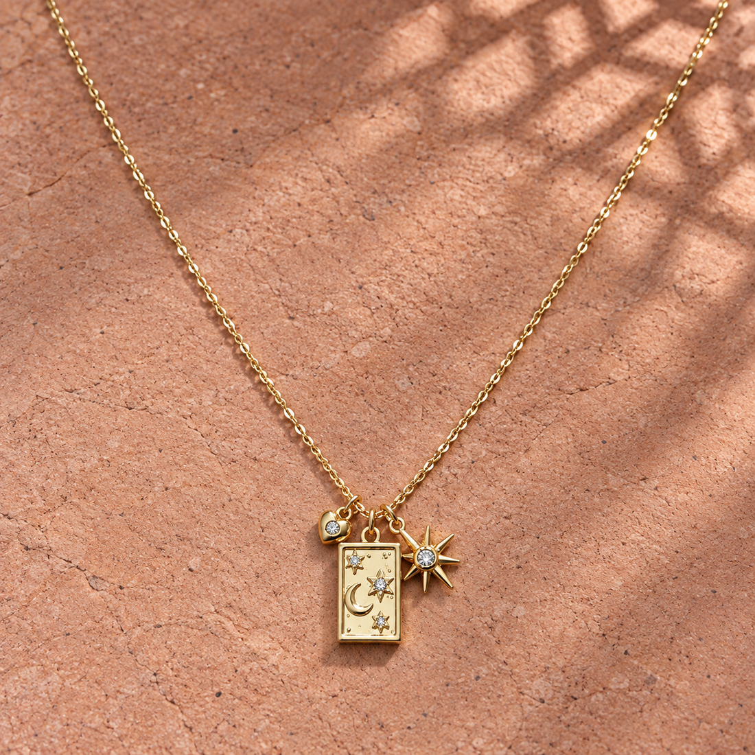 Gold-tone 316L stainless steel necklace with a rectangular charm engraved with moon and stars, plus a crystal-set star and small crystal bead