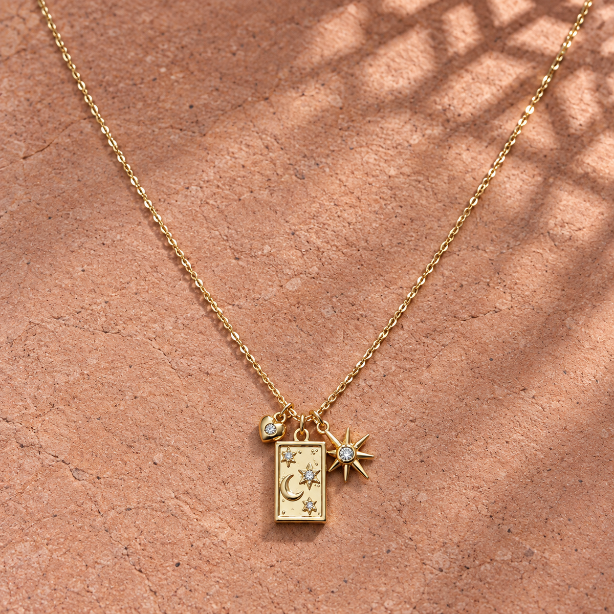 Gold-tone 316L stainless steel necklace with a rectangular charm engraved with moon and stars, plus a crystal-set star and small crystal bead