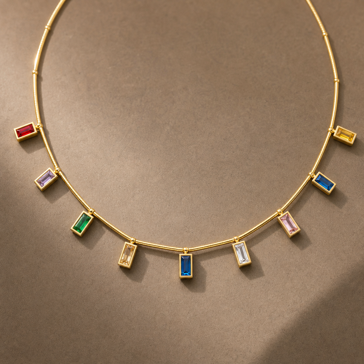 Gold-tone 304 stainless steel necklace with a thin rigid bar chain and nine bezel-set rectangular stones in red, green, blue, pink, yellow and white