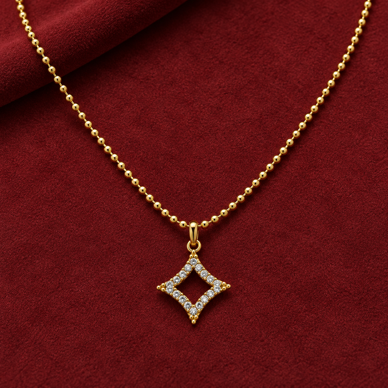 Gold-tone 304 stainless steel ball-chain necklace with an open diamond-shaped pendant set with clear stones, laid flat on a red suede surface