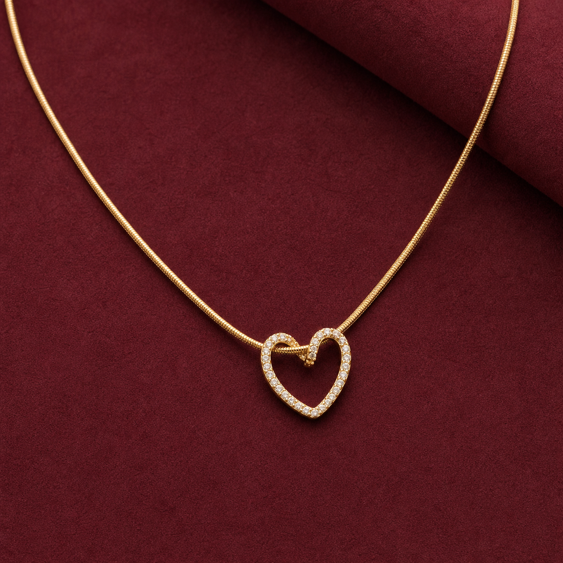 Gold-tone 304 stainless steel necklace with a fine snake chain and an open heart pendant set with clear stones, shown on a dark red surface