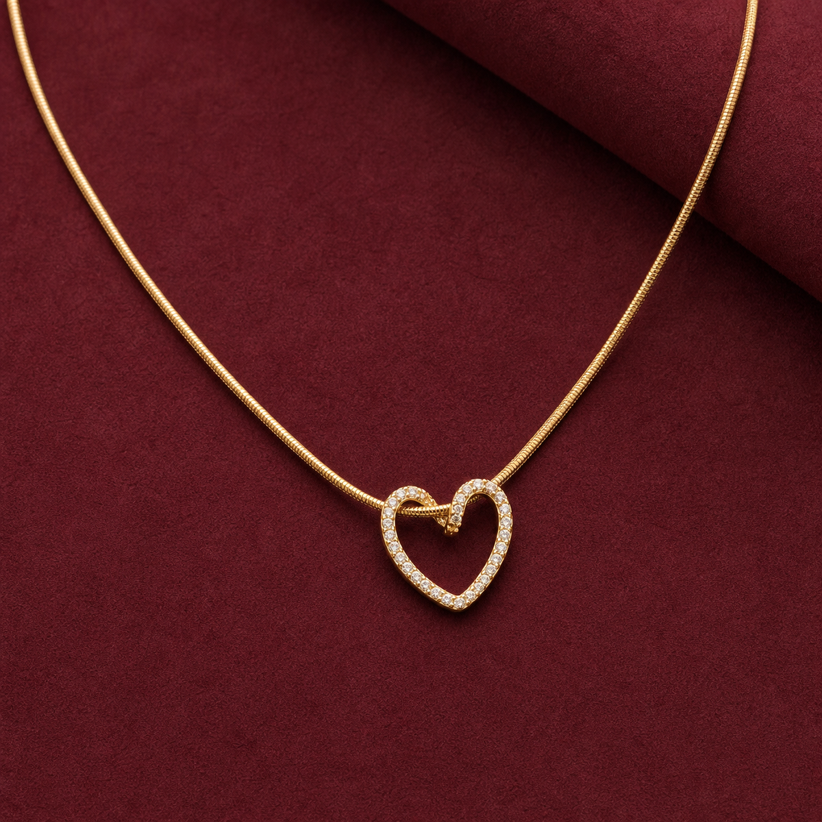 Gold-tone 304 stainless steel necklace with a fine snake chain and an open heart pendant set with clear stones, on a maroon surface