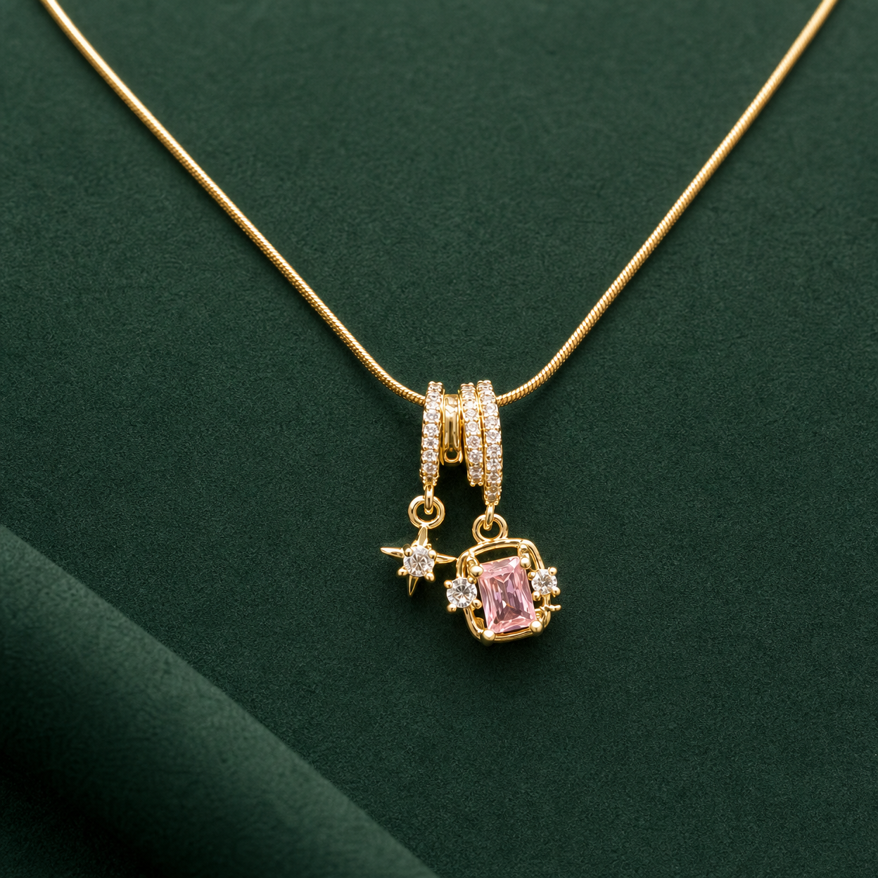 Gold-tone 304 stainless steel snake chain necklace with a pendant of a pink rectangular stone, a star charm and clear stones on a green background