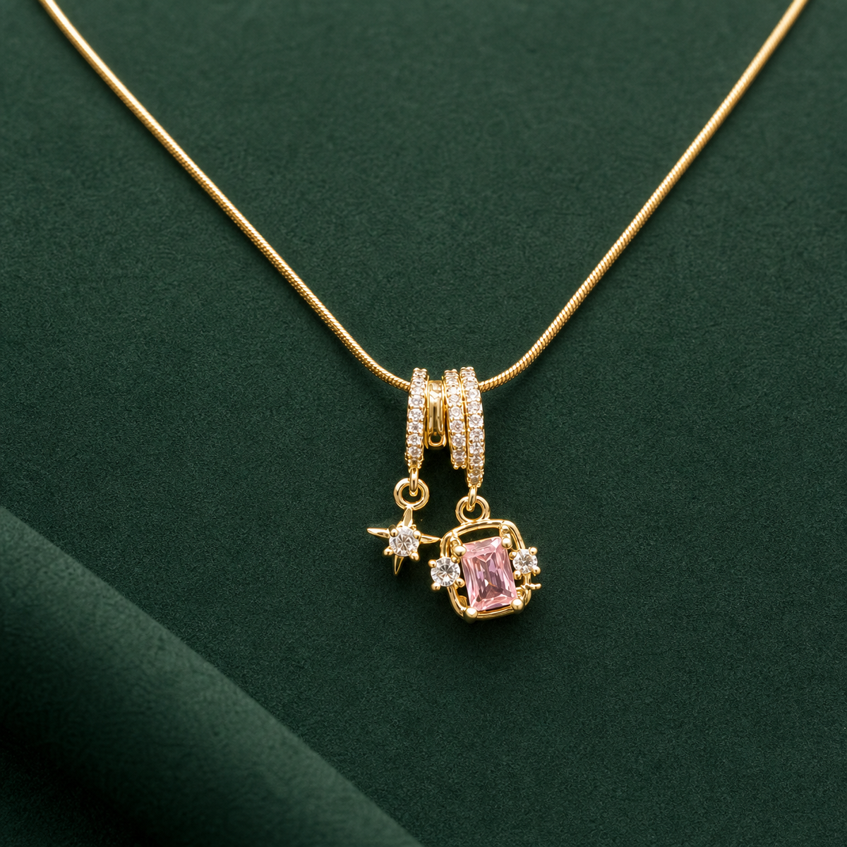 Gold-tone 304 stainless steel snake chain necklace with a pendant of a pink rectangular stone, a star charm and clear stones on a green background