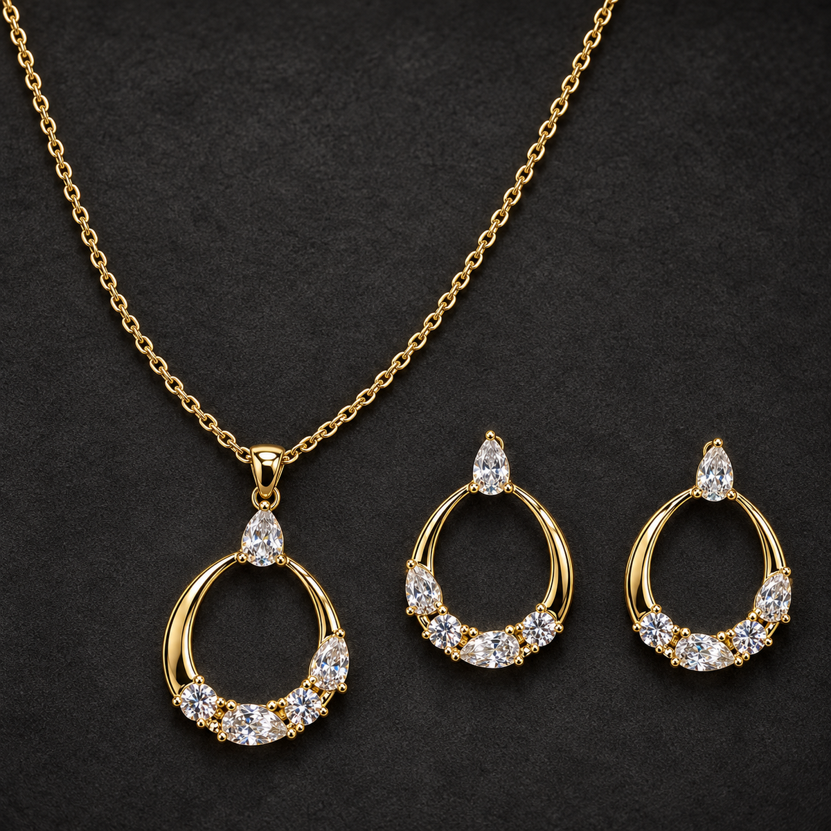 Gold-tone 316L stainless steel necklace and earring set with open teardrop pendants set with clear crystal stones, shown laid out on dark background