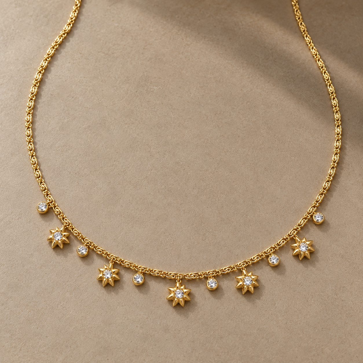 Gold-tone 316L stainless steel necklace with a fine chain and a row of star-shaped pendants alternating with round clear stones, laid flat
