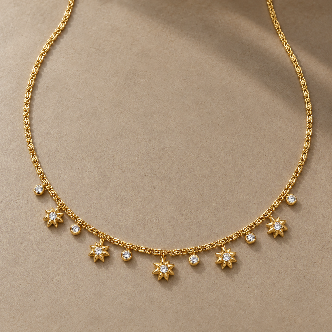 Gold-tone 316L stainless steel necklace with a fine chain and a row of star-shaped pendants alternating with round clear stones, laid flat