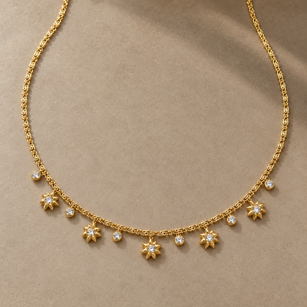 Gold-tone 316L stainless steel necklace with a fine chain and a row of star-shaped pendants alternating with round clear stones, laid flat