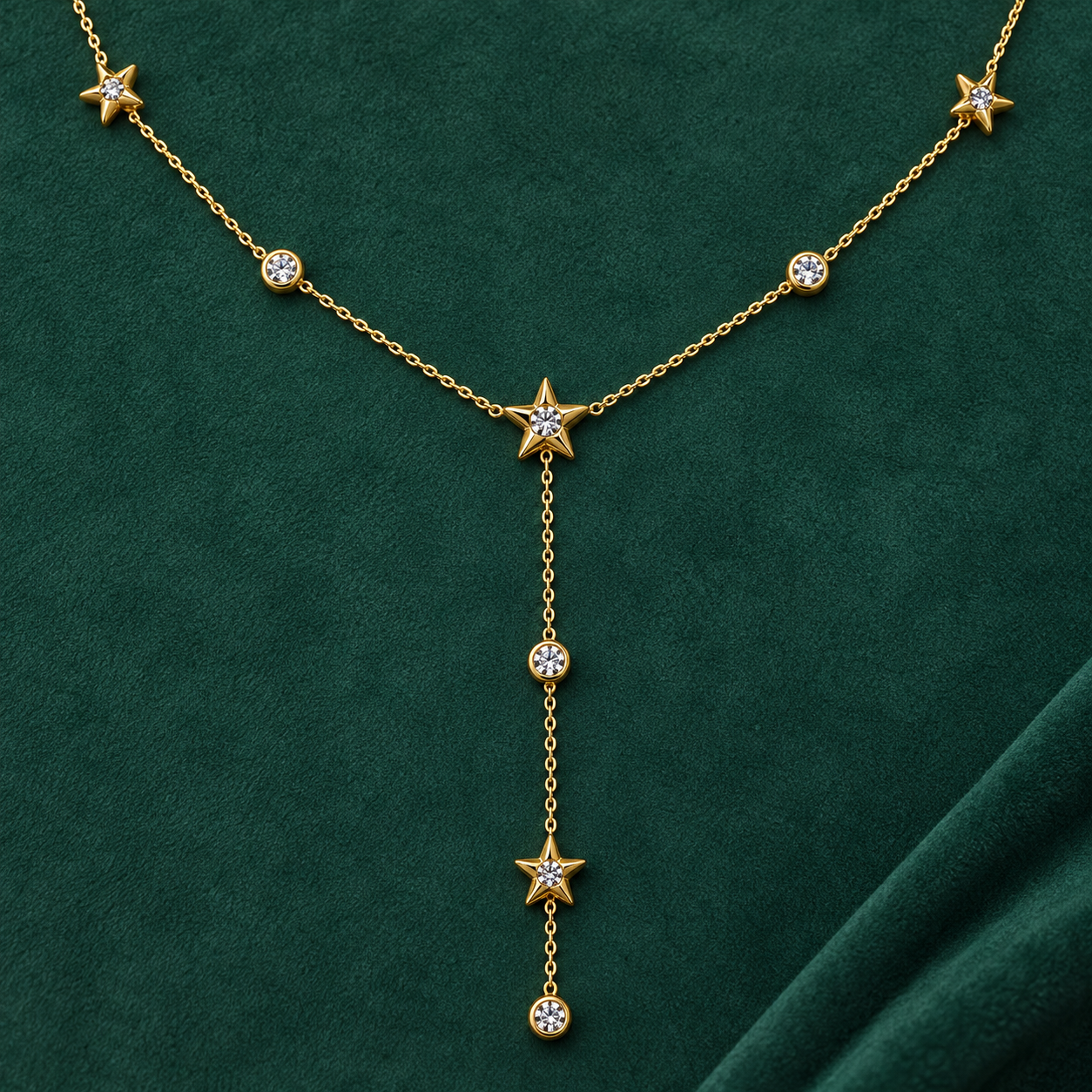 Gold-tone 316L stainless steel necklace with star motifs and clear stones on a fine chain, with a lariat drop on dark green fabric