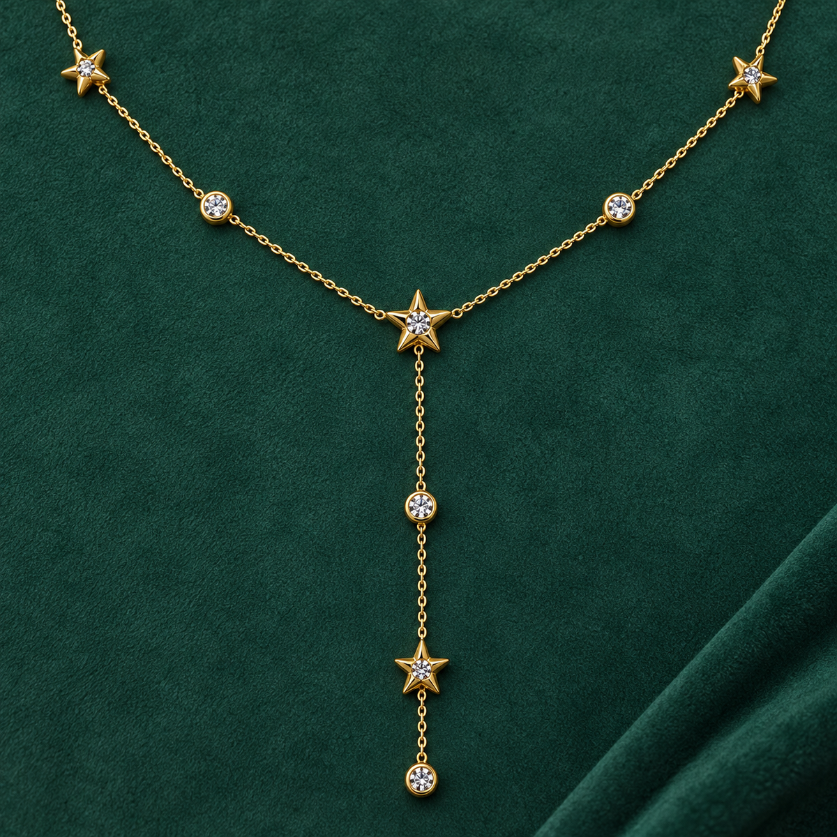 Gold-tone 316L stainless steel necklace with star motifs and clear stones on a fine chain, with a lariat drop on dark green fabric