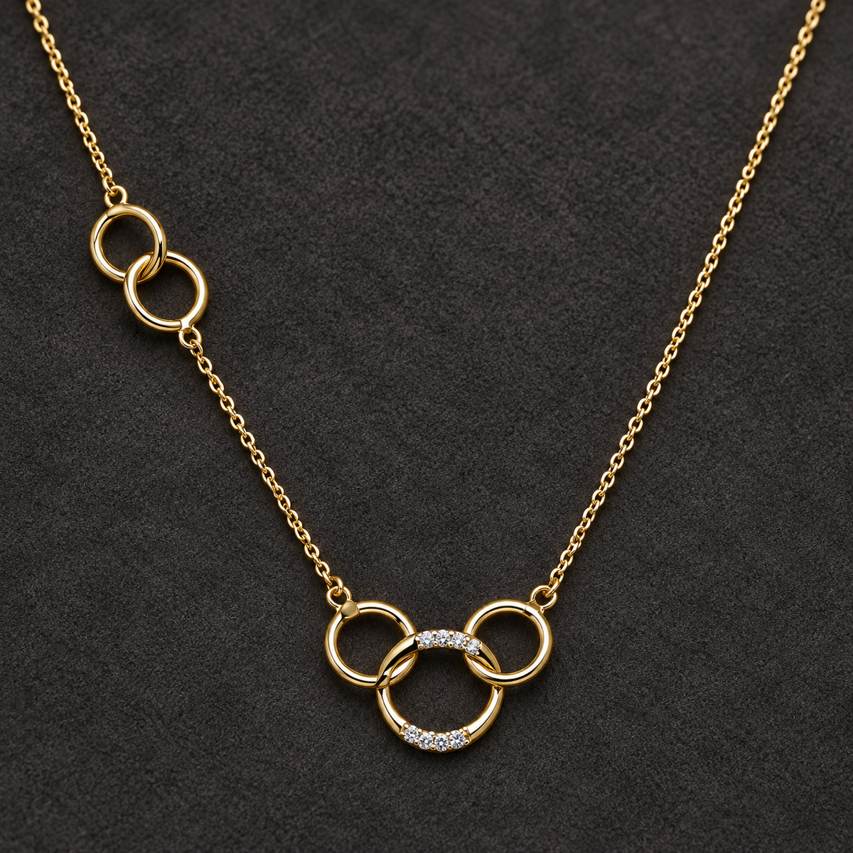 Gold-tone 316L stainless steel necklace with interlinked rings, two with crystal pavé, on a dark background