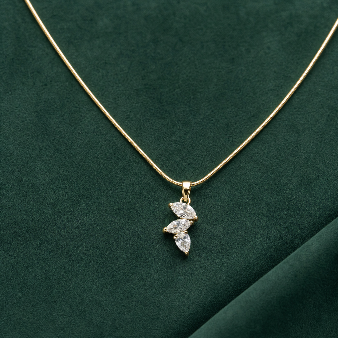 Gold-tone 316L stainless steel snake chain necklace with a pendant of three marquise and pear-cut clear stones, laid flat on green suede