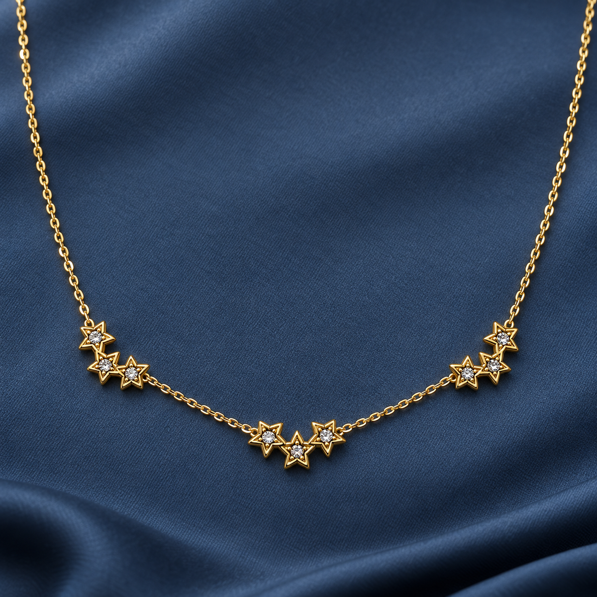 Gold-tone 316L stainless steel necklace with a fine chain and clusters of small star pendants set with clear stones, laid on dark blue fabric