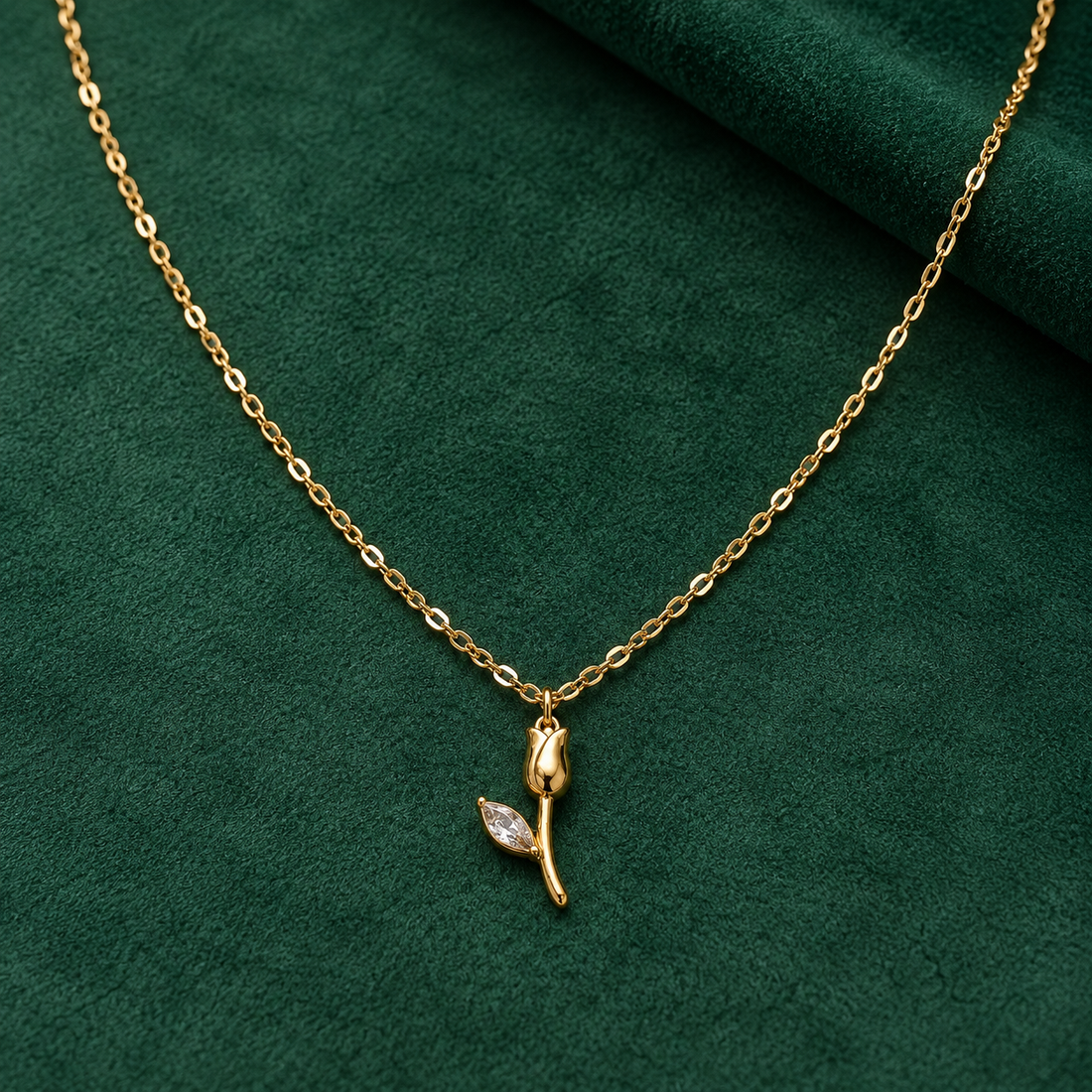 Gold-tone 304 stainless steel necklace with a fine cable chain and a tulip pendant with a marquise crystal leaf, laid flat on green fabric