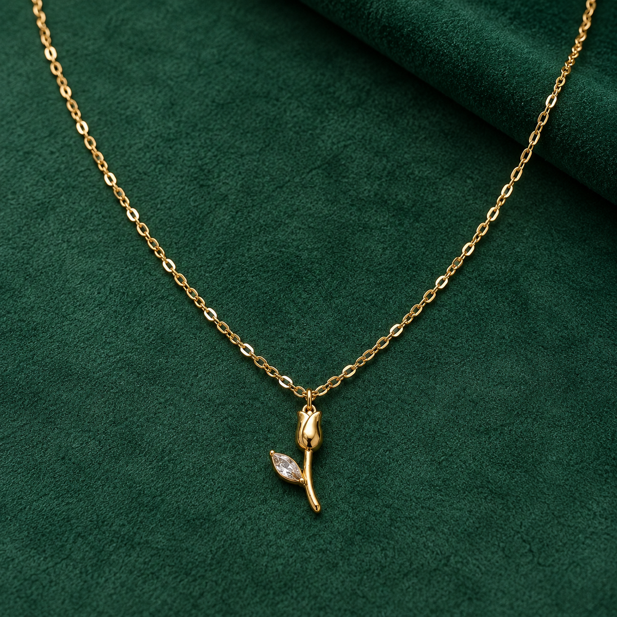 Gold-tone 304 stainless steel necklace with a fine cable chain and a tulip pendant with a marquise crystal leaf, laid flat on green fabric