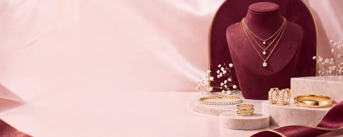 Gold-tone layered necklaces on a maroon velvet bust, with crystal hoop earrings, a tennis bracelet, stacked rings and a bangle on marble podiums