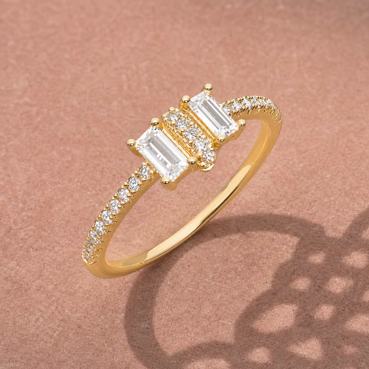 Gold-tone 316L ring with three baguette-cut white stones and a row of small round stones along the band, on a rose-coloured surface