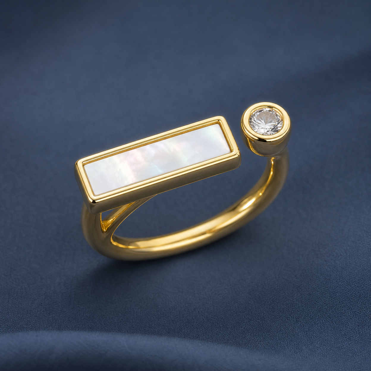 Gold-tone 316L stainless steel open ring with a mother-of-pearl bar and a round crystal-set end, on a dark blue backdrop