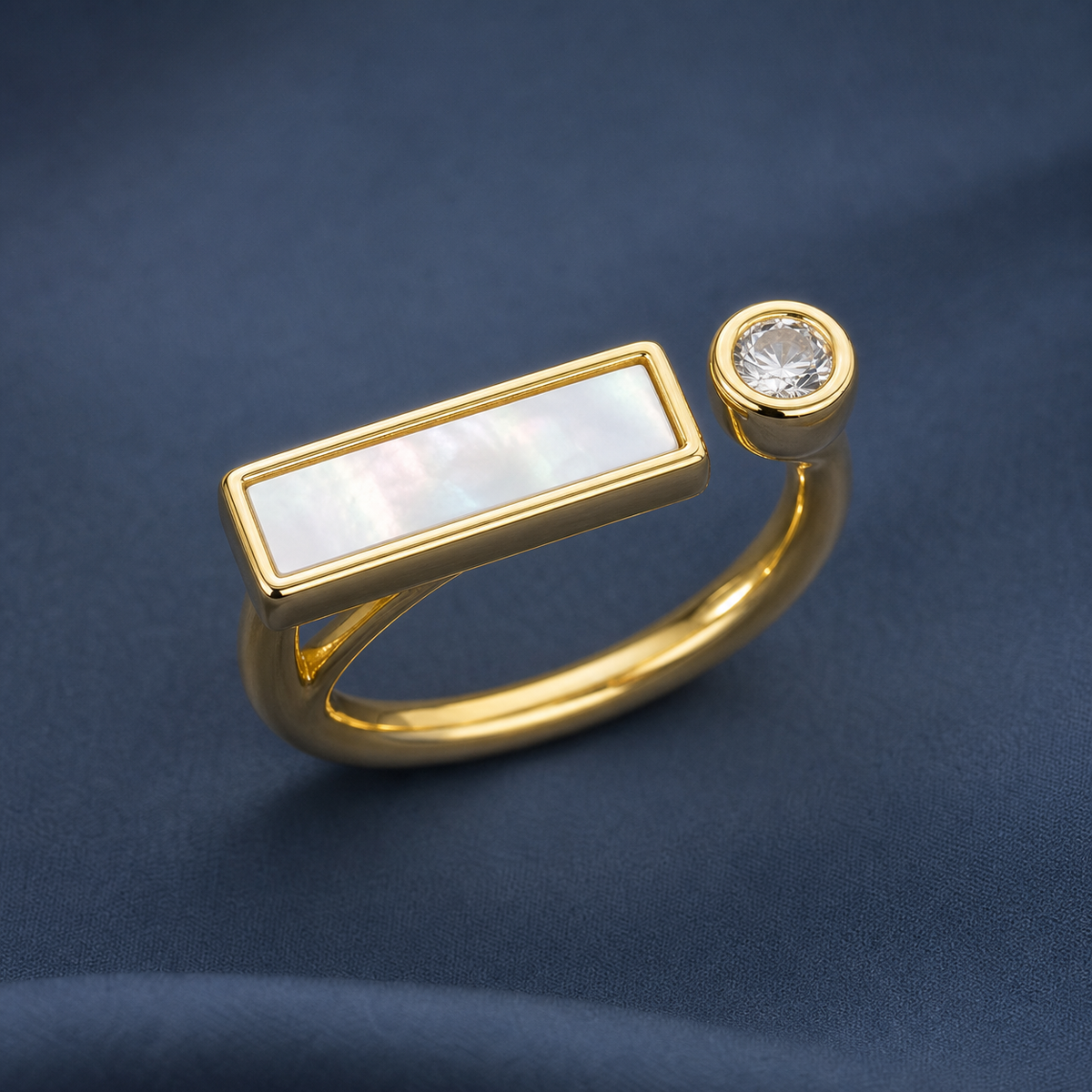 Gold-tone 316L stainless steel open ring with a mother-of-pearl bar and a round crystal-set end, on a dark blue backdrop
