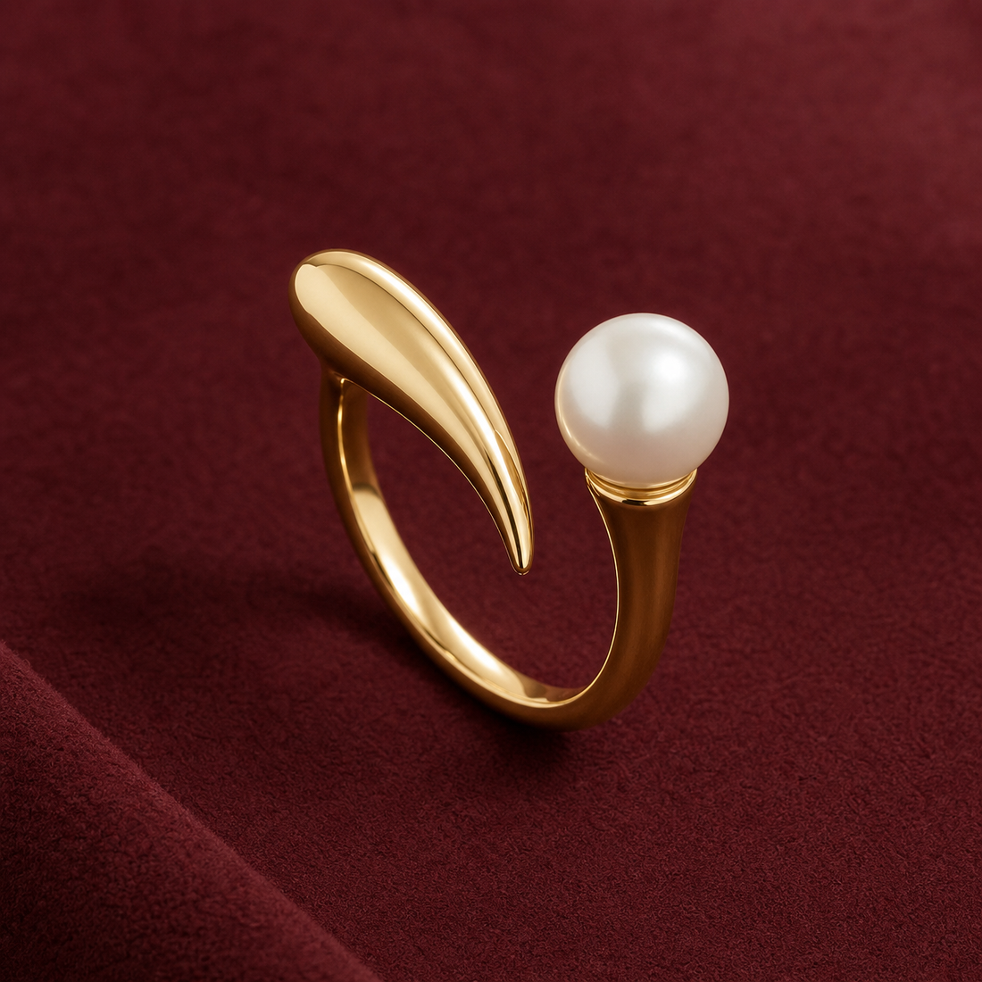 Gold-tone 316L stainless steel open ring with a tapered curved bar and a white pearl set at the other end, on a maroon fabric surface